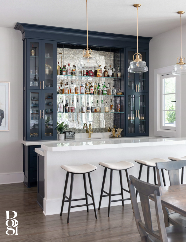upscale breakfast bar with four white stools and a fully stocked bar on the wall behind it and dark blue painted cabinets