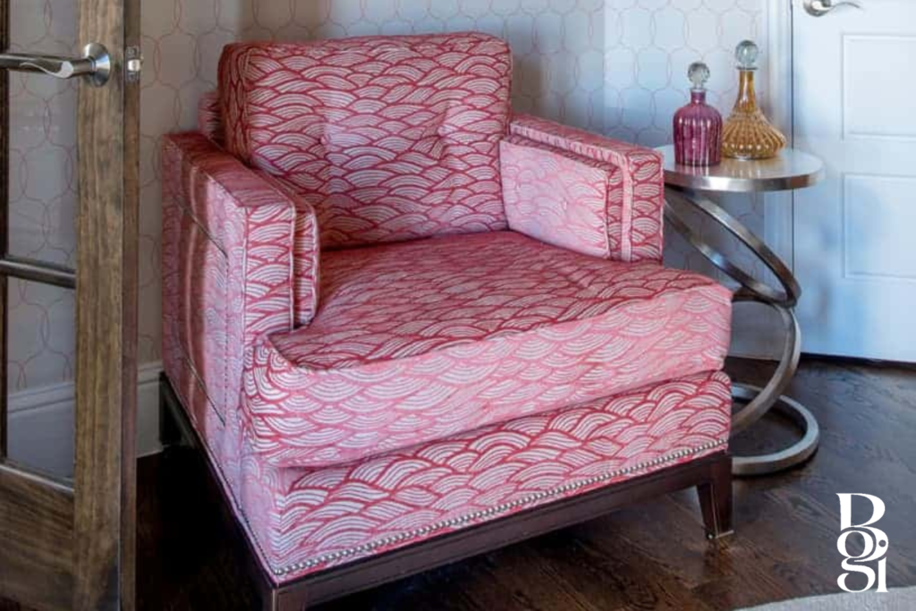 red arm chair with accompanying accessories of a gold swirl end table and blown glass jars